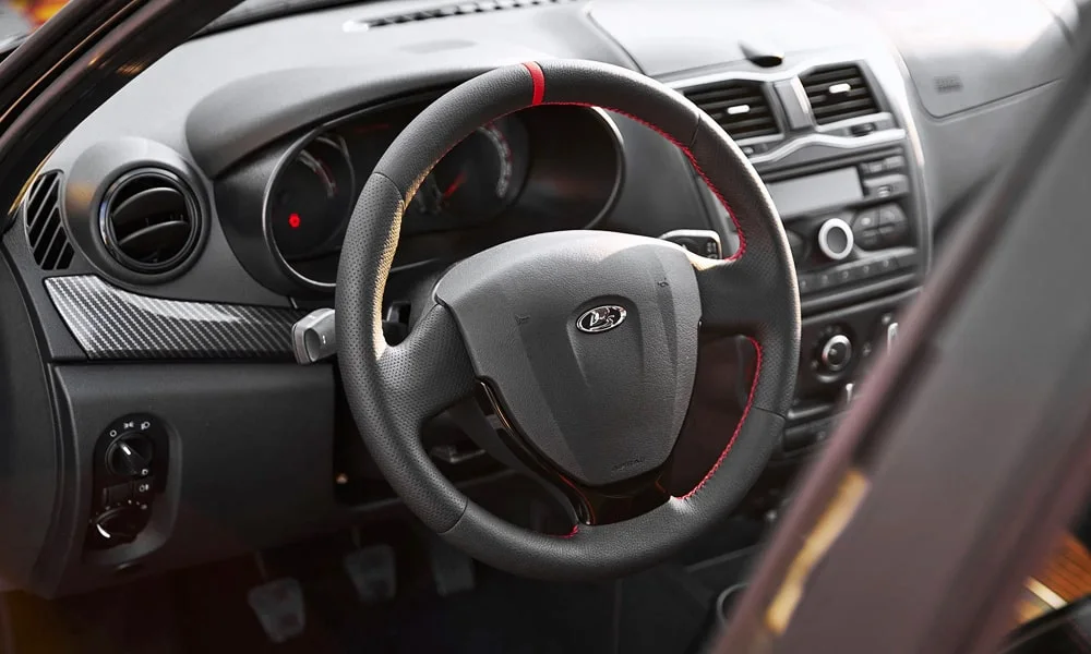 Фото LADA Granta Sport Лифтбек (2023) — руль. Обшивка обода и компоновка спиц крупным планом. Клавиши на спицах управляют медиа, круизом и ассистентами — руки остаются на руле LADA Granta Sport Лифтбек (2023) — руль