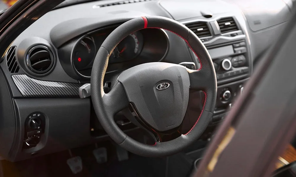 Фото LADA Granta Sport (2023) — руль. Обшивка обода и компоновка спиц крупным планом. Клавиши на спицах управляют медиа, круизом и ассистентами — руки остаются на руле LADA Granta Sport (2023) — руль