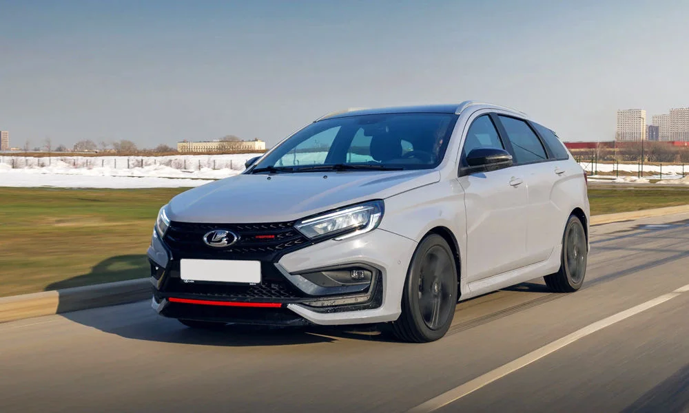 Фото LADA Vesta SW Sport (2026) — вид спереди, фото 7. Передок в белом исполнении — крупная светотехника и выразительный бампер. Рисунок ходовых огней — подпись модели, по нему её узнают в потоке LADA Vesta SW Sport (2026) — вид спереди, фото 7