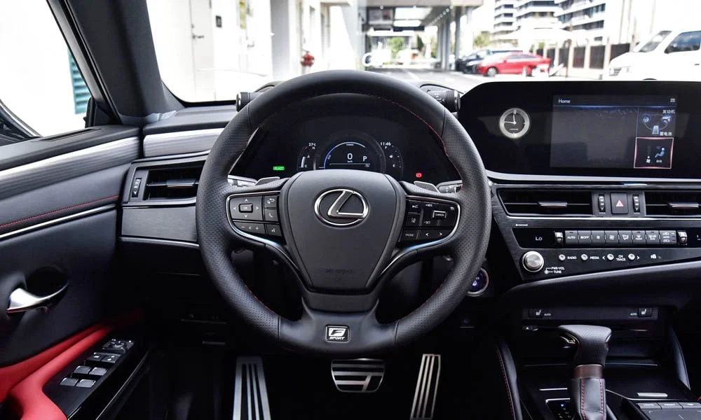 Фото Lexus ES 250 — руль. Обшивка обода и компоновка спиц крупным планом. Клавиши на спицах управляют медиа, круизом и ассистентами — руки остаются на руле Lexus ES 250 — руль