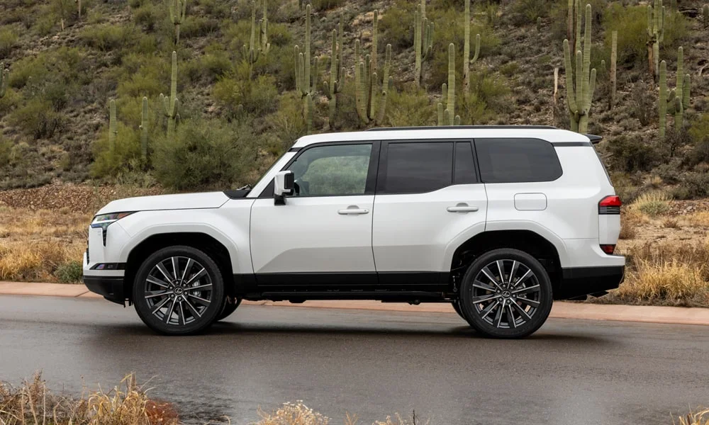 Фото Lexus GX 550 (2024) — вид сбоку, фото 3. Сбоку читаются линия остекления и характер выштамповок на белом кузове Lexus GX 550 (2024) — вид сбоку, фото 3