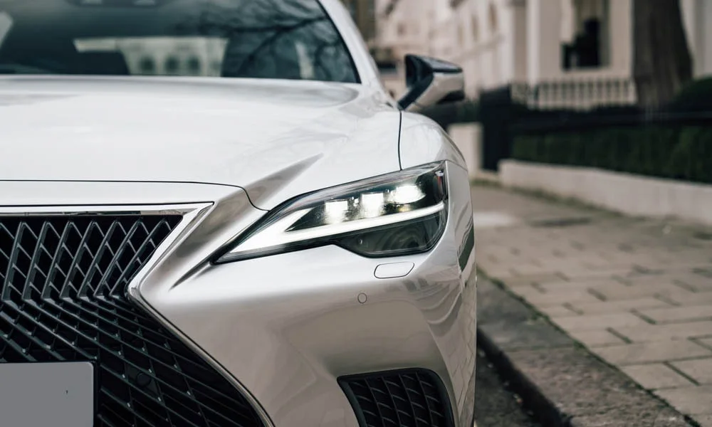Фото Lexus LS 350 — вид спереди, фото 12. Белый кузов, строгая симметрия оптики — базовый ракурс знакомства с дизайном. Рисунок ходовых огней — подпись модели, по нему её узнают в потоке Lexus LS 350 — вид спереди, фото 12