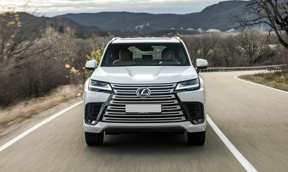 Фото Lexus LX 500d (2022) — вид спереди, фото 5. Белый кузов, строгая симметрия оптики — базовый ракурс знакомства с дизайном. Дневные ходовые огни включаются автоматически с запуском Lexus LX 500d (2022) — вид спереди, фото 5