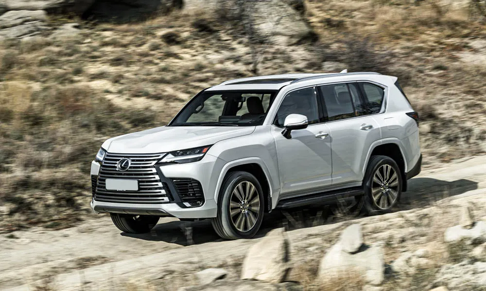 Фото Lexus LX 500d (2022) — вид спереди, фото 8. Передок в белом исполнении — крупная светотехника и выразительный бампер. Рисунок ходовых огней — подпись модели, по нему её узнают в потоке Lexus LX 500d (2022) — вид спереди, фото 8