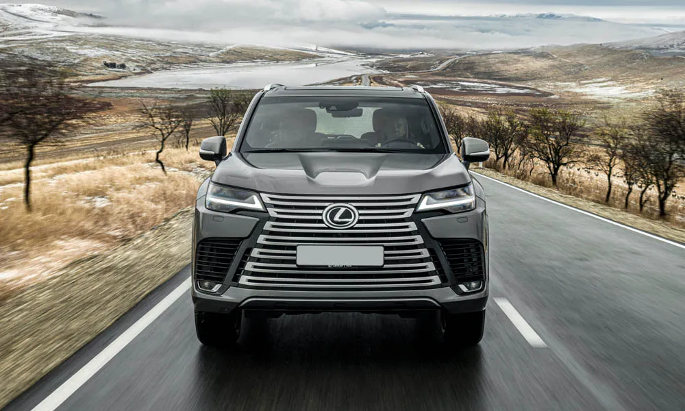 Фото Lexus LX 600 (2022) — вид спереди, фото 8. Серый кузов, строгая симметрия оптики — базовый ракурс знакомства с дизайном. Рисунок ходовых огней — подпись модели, по нему её узнают в потоке Lexus LX 600 (2022) — вид спереди, фото 8