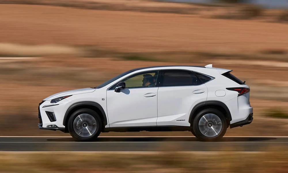 Фото Lexus NX 300h — вид сбоку, фото 2. Сбоку читаются линия остекления и характер выштамповок на белом кузове. Хромированные или чёрные молдинги окон отличают комплектации Lexus NX 300h — вид сбоку, фото 2