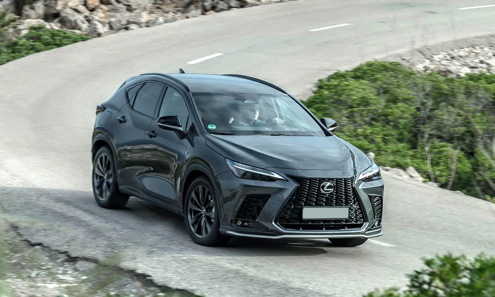 Фото Lexus NX 450h (2024) — вид спереди, фото 7. Кузов в чёрном цвете: рисунок оптики и решётки задаёт узнаваемое «лицо» модели. Рисунок ходовых огней — подпись модели, по нему её узнают в потоке Lexus NX 450h (2024) — вид спереди, фото 7