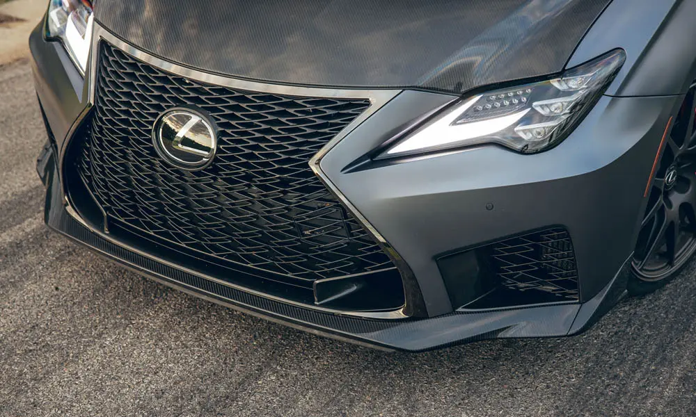 Фото Lexus RC F (2024) — вид спереди, фото 6. Кузов в сером цвете: рисунок оптики и решётки задаёт узнаваемое «лицо» модели. Рисунок ходовых огней — подпись модели, по нему её узнают в потоке Lexus RC F (2024) — вид спереди, фото 6