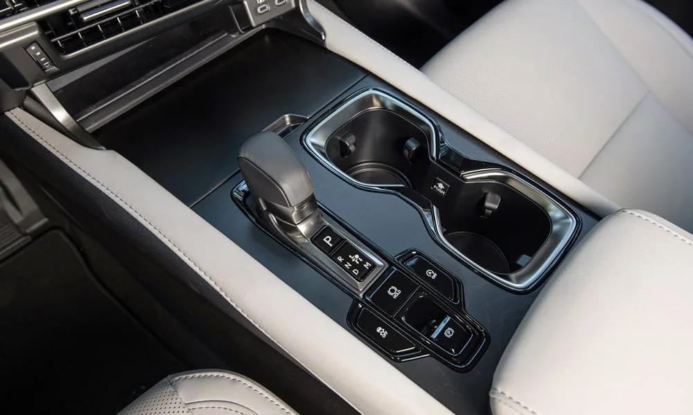 Фото Lexus RX 350h (2024) — центральная консоль. Бокс консоли открыт: организация хранения между креслами. Продуманное хранение: подстаканники, ниша для смартфона и глубокий бокс Lexus RX 350h (2024) — центральная консоль