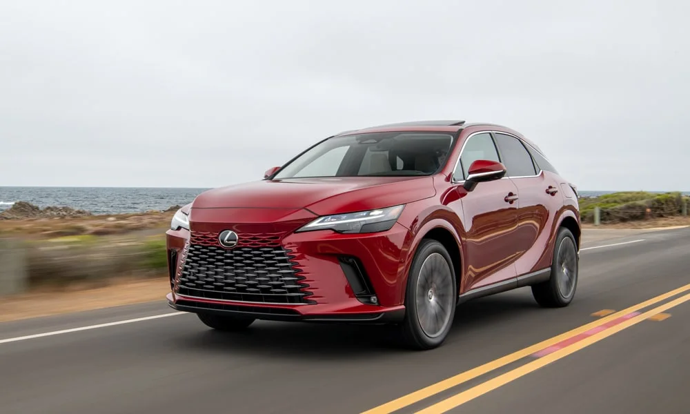Фото Lexus RX 450h (2024) — вид спереди, фото 3. Кузов в красном цвете: рисунок оптики и решётки задаёт узнаваемое «лицо» модели. Дневные ходовые огни включаются автоматически с запуском Lexus RX 450h (2024) — вид спереди, фото 3