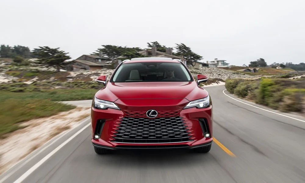 Фото Lexus RX 450h (2024) — вид спереди, фото 4. Красный кузов, строгая симметрия оптики — базовый ракурс знакомства с дизайном. Рисунок ходовых огней — подпись модели, по нему её узнают в потоке Lexus RX 450h (2024) — вид спереди, фото 4