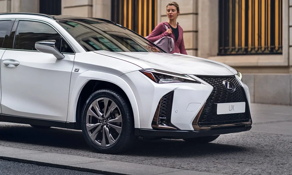 Фото Lexus UX 250h (2024) — вид спереди, фото 6. Передок в белом исполнении — крупная светотехника и выразительный бампер. Рисунок ходовых огней — подпись модели, по нему её узнают в потоке Lexus UX 250h (2024) — вид спереди, фото 6