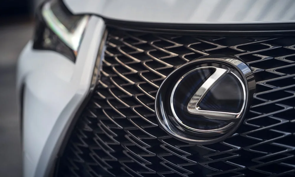 Фото Lexus UX 250h (2024) — решётка радиатора. Рисунок решётки: сетка, ламели или глухая панель у электроверсий. За решёткой у многих комплектаций стоит радар адаптивного круиз-контроля Lexus UX 250h (2024) — решётка радиатора