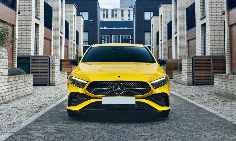 Фото Mercedes-Benz A-Class (2024) — вид спереди, фото 3. Кузов в жёлтом цвете: рисунок оптики и решётки задаёт узнаваемое «лицо» модели. Рисунок ходовых огней — подпись модели, по нему её узнают в потоке Mercedes-Benz A-Class (2024) — вид спереди, фото 3