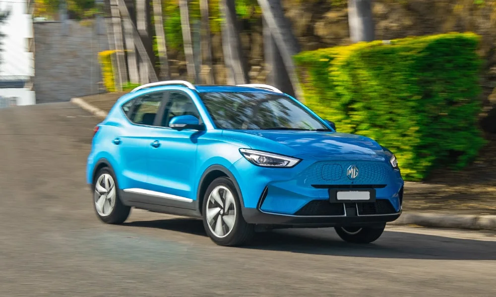 Фото MG ZS EV (2024) — вид спереди, фото 4. Передок в синем исполнении — крупная светотехника и выразительный бампер. Рисунок ходовых огней — подпись модели, по нему её узнают в потоке MG ZS EV (2024) — вид спереди, фото 4