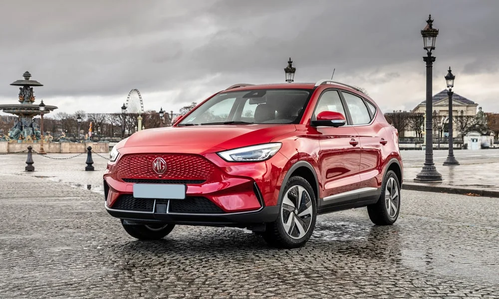Фото MG ZS EV (2024) — вид спереди, фото 5. Красный кузов, строгая симметрия оптики — базовый ракурс знакомства с дизайном. Дневные ходовые огни включаются автоматически с запуском MG ZS EV (2024) — вид спереди, фото 5