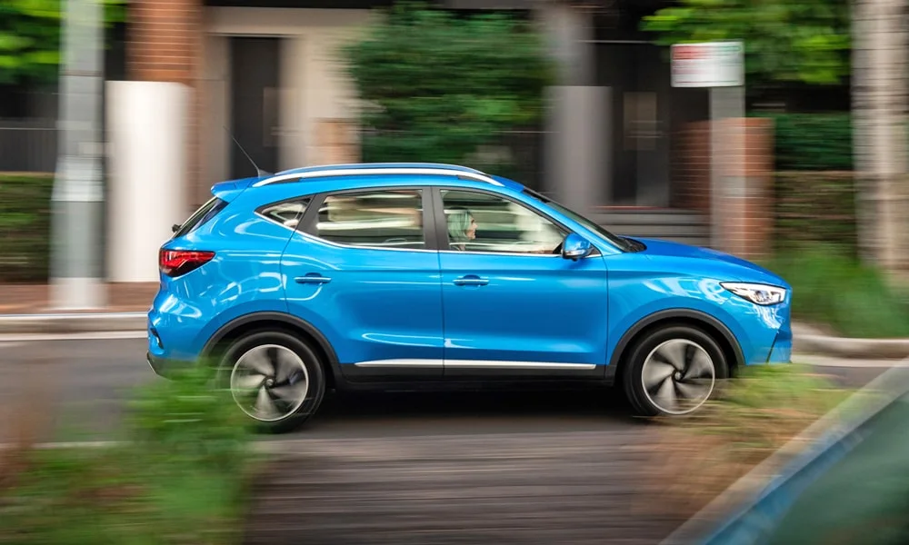 Фото MG ZS EV (2024) — вид сбоку, фото 2. Сбоку читаются линия остекления и характер выштамповок на синем кузове MG ZS EV (2024) — вид сбоку, фото 2