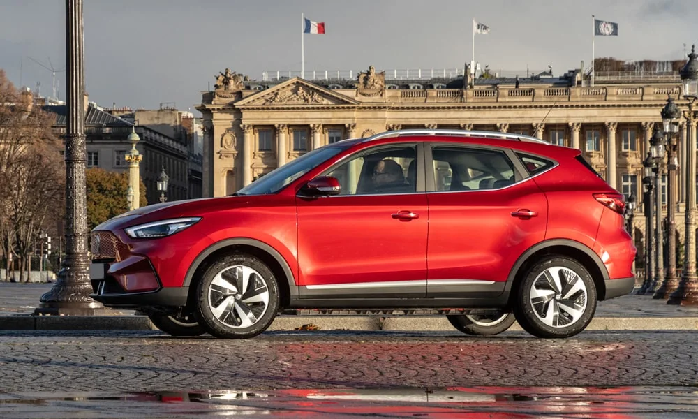 Фото MG ZS EV (2024) — вид сбоку, фото 4. Профиль в красном цвете: соотношение колёсной базы и свесов. Длинная база — простор второго ряда; короткие свесы упрощают парковку MG ZS EV (2024) — вид сбоку, фото 4