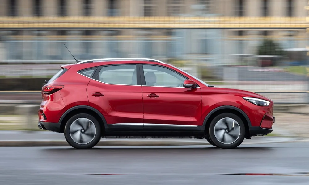 Фото MG ZS EV (2024) — вид сбоку, фото 6. Сбоку читаются линия остекления и характер выштамповок на красном кузове. Длинная база — простор второго ряда; короткие свесы упрощают парковку MG ZS EV (2024) — вид сбоку, фото 6