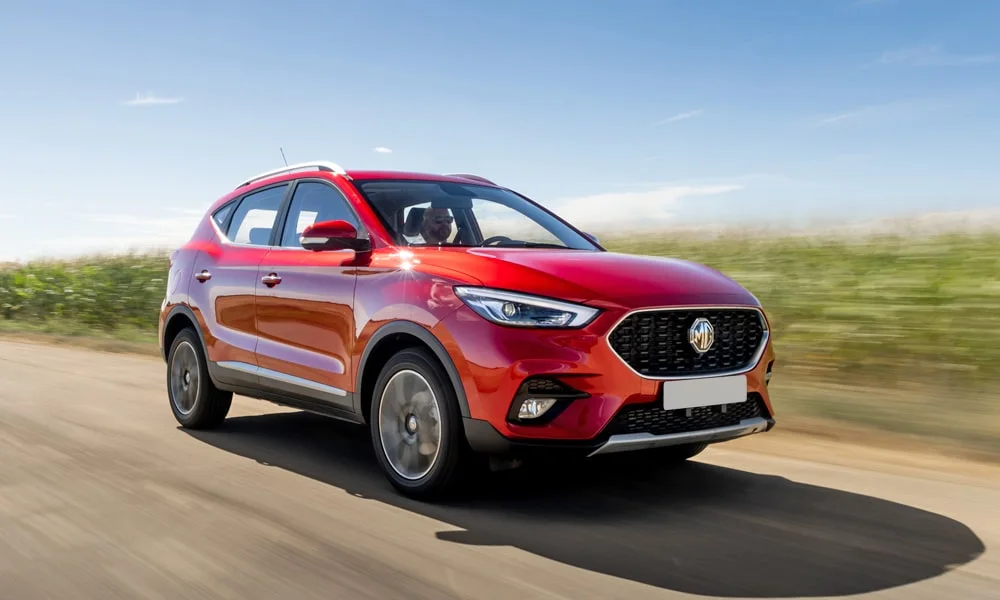 Фото MG ZS (2024) — вид спереди, фото 3. Кузов в красном цвете: рисунок оптики и решётки задаёт узнаваемое «лицо» модели. Рисунок ходовых огней — подпись модели, по нему её узнают в потоке MG ZS (2024) — вид спереди, фото 3