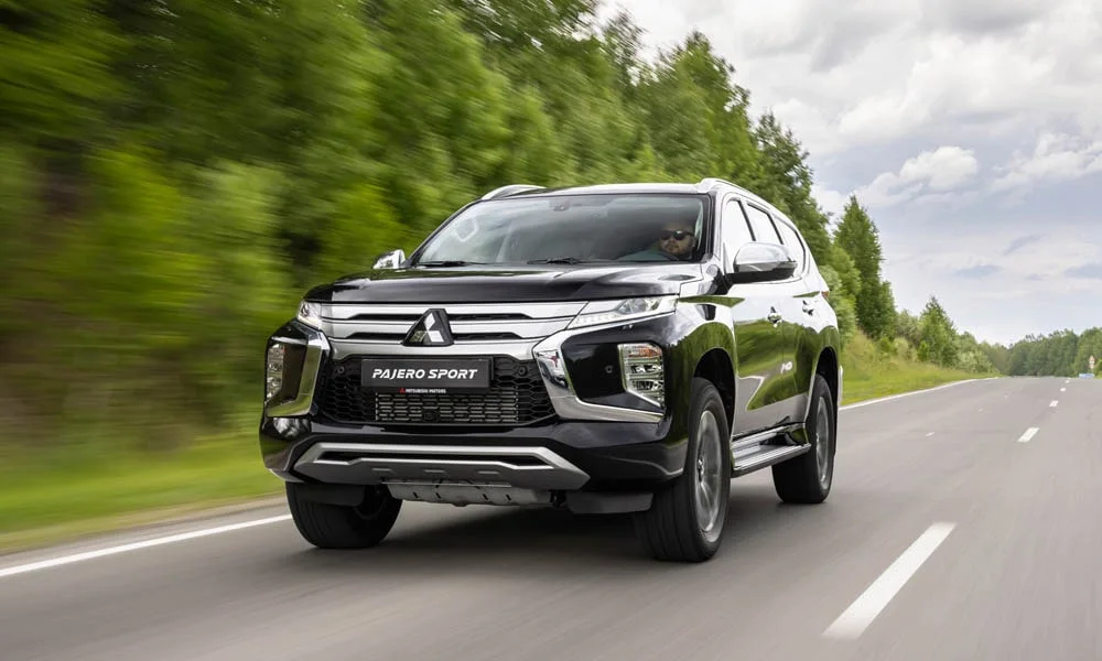 Фото Mitsubishi Pajero Sport — вид спереди, фото 6. Кузов в чёрном цвете: рисунок оптики и решётки задаёт узнаваемое «лицо» модели. Рисунок ходовых огней — подпись модели, по нему её узнают в потоке Mitsubishi Pajero Sport — вид спереди, фото 6