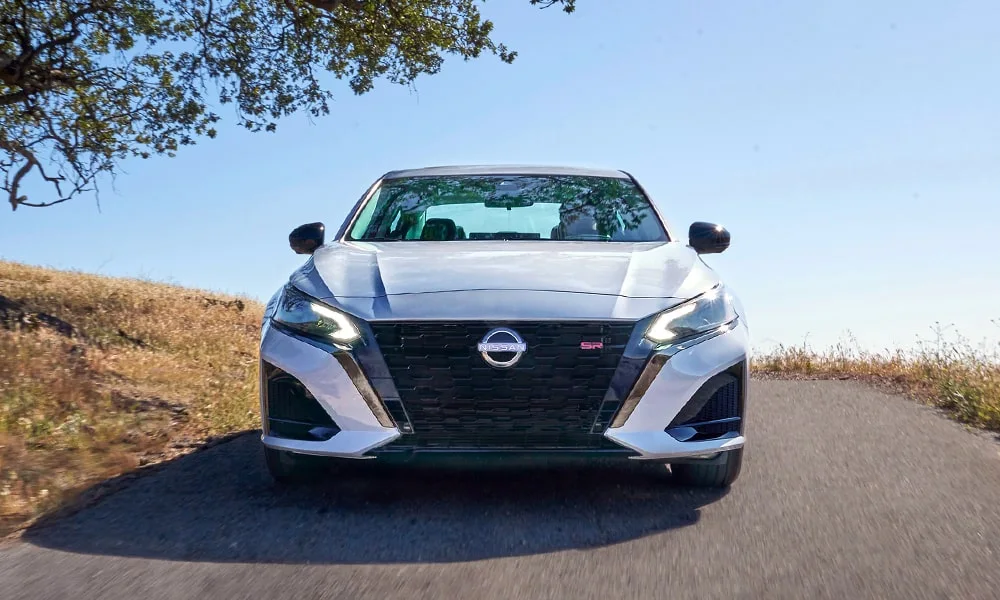 Фото Nissan Altima (2024) — вид спереди, фото 5. Серебристый кузов, строгая симметрия оптики — базовый ракурс знакомства с дизайном. Рисунок ходовых огней — подпись модели, по нему её узнают в потоке Nissan Altima (2024) — вид спереди, фото 5