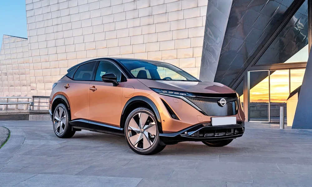Фото Nissan Ariya (2024) — вид спереди, фото 6. Кузов в коричневом цвете: рисунок оптики и решётки задаёт узнаваемое «лицо» модели. Дневные ходовые огни включаются автоматически с запуском Nissan Ariya (2024) — вид спереди, фото 6