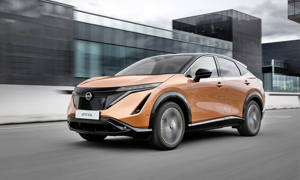 Фото Nissan Ariya (2024) — вид спереди, фото 9. Кузов в оранжевом цвете: рисунок оптики и решётки задаёт узнаваемое «лицо» модели Nissan Ariya (2024) — вид спереди, фото 9