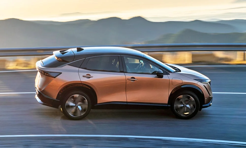 Фото Nissan Ariya (2024) — вид сбоку, фото 2. Профиль в коричневом цвете: соотношение колёсной базы и свесов. Хромированные или чёрные молдинги окон отличают комплектации Nissan Ariya (2024) — вид сбоку, фото 2