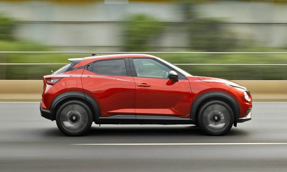 Фото Nissan Juke (2024) — вид сбоку, фото 2. Красный кузов в профиль — пропорции, высота посадки и дизайн дисков Nissan Juke (2024) — вид сбоку, фото 2