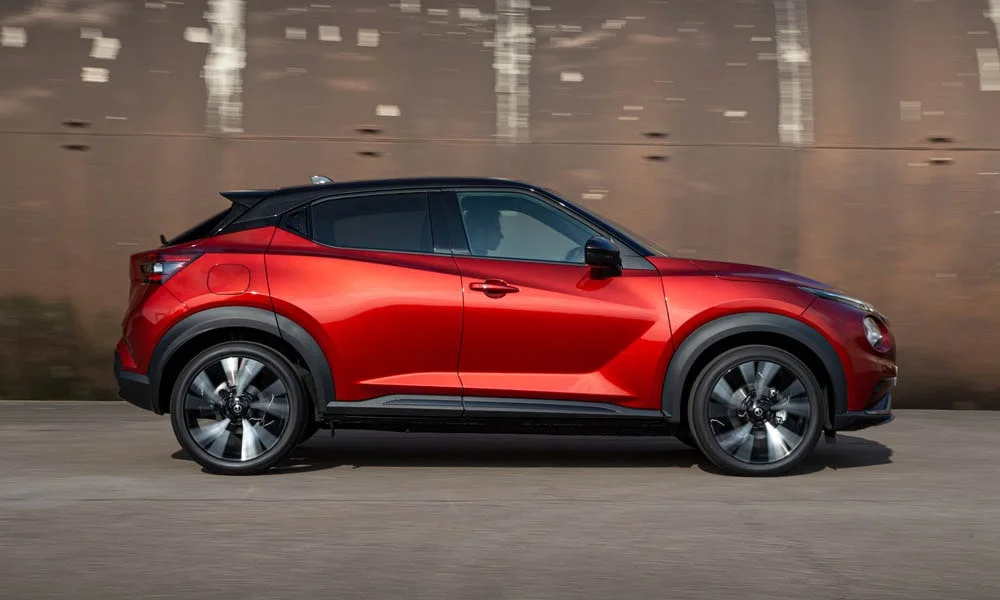 Фото Nissan Juke (2024) — вид сбоку, фото 3. Сбоку читаются линия остекления и характер выштамповок на красном кузове. Хромированные или чёрные молдинги окон отличают комплектации Nissan Juke (2024) — вид сбоку, фото 3