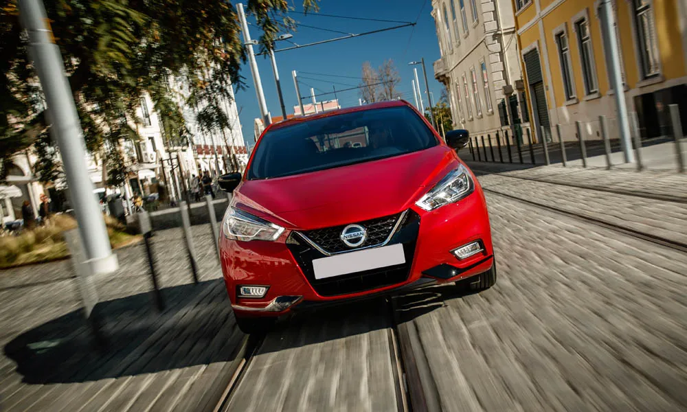 Фото Nissan Micra — вид спереди, фото 6. Кузов в красном цвете: рисунок оптики и решётки задаёт узнаваемое «лицо» модели. Рисунок ходовых огней — подпись модели, по нему её узнают в потоке Nissan Micra — вид спереди, фото 6
