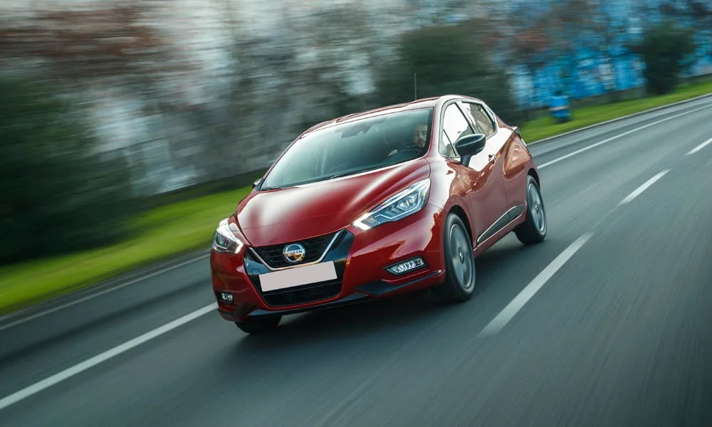 Фото Nissan Micra — вид спереди, фото 13. Кузов в красном цвете: рисунок оптики и решётки задаёт узнаваемое «лицо» модели. Рисунок ходовых огней — подпись модели, по нему её узнают в потоке Nissan Micra — вид спереди, фото 13