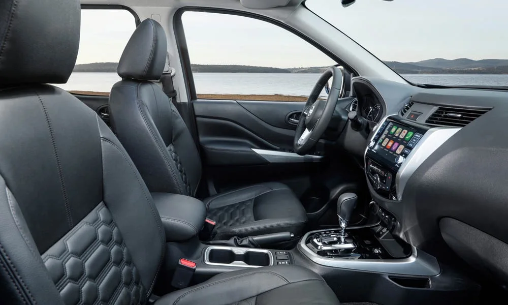 Фото Nissan Navara — интерьер. Интерьер с тёмной отделкой — видно сочетание материалов панели и кресел. Светлая гамма зрительно расширяет салон, тёмная — практичнее в уходе Nissan Navara — интерьер