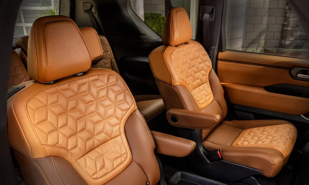 Фото Nissan Patrol (2024) — задние сиденья. Задний диван в стёганой коже: посадка и центральный подлокотник. Спинки складываются под длинные грузы у большинства версий Nissan Patrol (2024) — задние сиденья
