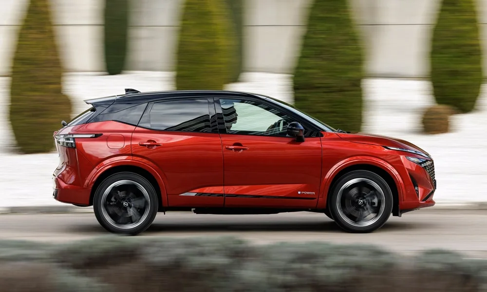 Фото Nissan Qashqai (2024) — вид сбоку, фото 5. Красный кузов в профиль — пропорции, высота посадки и дизайн дисков. Хромированные или чёрные молдинги окон отличают комплектации Nissan Qashqai (2024) — вид сбоку, фото 5