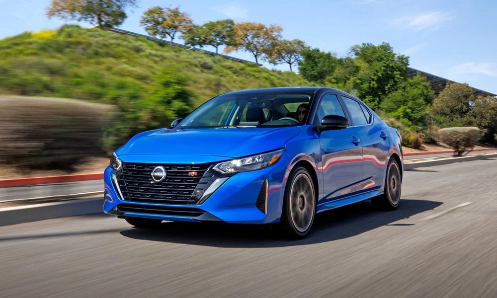 Фото Nissan Sentra — вид спереди, фото 5. Кузов в синем цвете: рисунок оптики и решётки задаёт узнаваемое «лицо» модели. Дневные ходовые огни включаются автоматически с запуском Nissan Sentra — вид спереди, фото 5