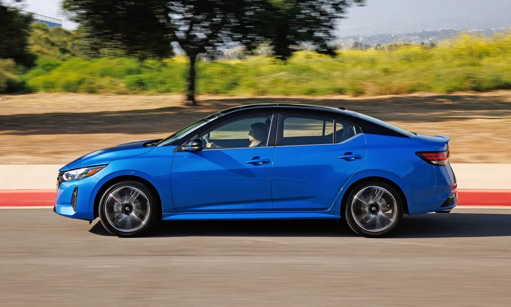 Фото Nissan Sentra — вид сбоку, фото 3. Сбоку читаются линия остекления и характер выштамповок на синем кузове. Хромированные или чёрные молдинги окон отличают комплектации Nissan Sentra — вид сбоку, фото 3