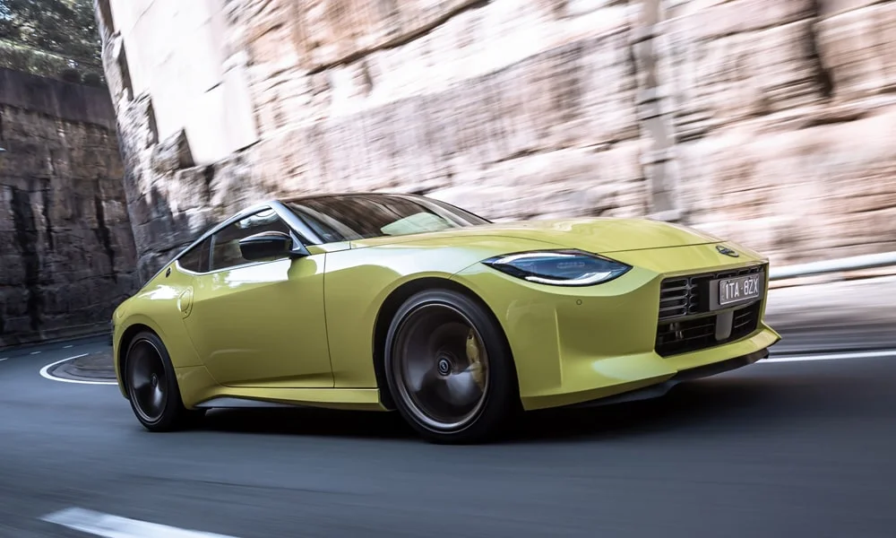Фото Nissan Z (2024) — вид спереди, фото 4. Кузов в жёлтом цвете: рисунок оптики и решётки задаёт узнаваемое «лицо» модели. Рисунок ходовых огней — подпись модели, по нему её узнают в потоке Nissan Z (2024) — вид спереди, фото 4