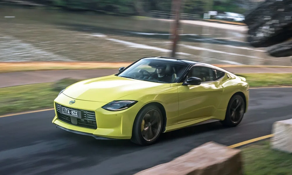 Фото Nissan Z (2024) — вид спереди, фото 5. Жёлтый кузов, строгая симметрия оптики — базовый ракурс знакомства с дизайном. Рисунок ходовых огней — подпись модели, по нему её узнают в потоке Nissan Z (2024) — вид спереди, фото 5