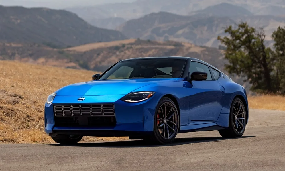 Фото Nissan Z (2024) — вид спереди, фото 8. Синий кузов, строгая симметрия оптики — базовый ракурс знакомства с дизайном. Рисунок ходовых огней — подпись модели, по нему её узнают в потоке Nissan Z (2024) — вид спереди, фото 8