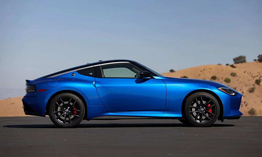 Фото Nissan Z (2024) — вид сбоку, фото 2. Профиль в синем цвете: соотношение колёсной базы и свесов. Хромированные или чёрные молдинги окон отличают комплектации Nissan Z (2024) — вид сбоку, фото 2