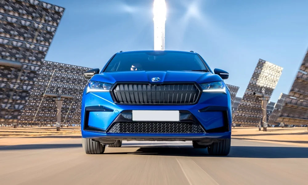 Фото Skoda Enyaq (2024) — вид спереди, фото 7. Синий кузов, строгая симметрия оптики — базовый ракурс знакомства с дизайном. Рисунок ходовых огней — подпись модели, по нему её узнают в потоке Skoda Enyaq (2024) — вид спереди, фото 7