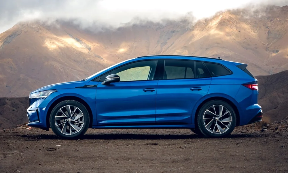 Фото Skoda Enyaq (2024) — вид сбоку, фото 4. Профиль в синем цвете: соотношение колёсной базы и свесов. Хромированные или чёрные молдинги окон отличают комплектации Skoda Enyaq (2024) — вид сбоку, фото 4
