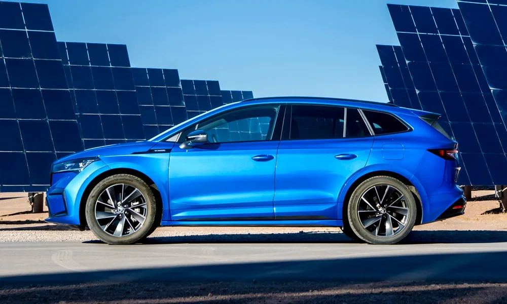 Фото Skoda Enyaq (2024) — вид сбоку, фото 5. Профиль в синем цвете: соотношение колёсной базы и свесов. Хромированные или чёрные молдинги окон отличают комплектации Skoda Enyaq (2024) — вид сбоку, фото 5