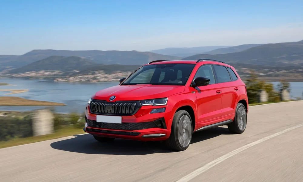 Фото Skoda Karoq (2024) — вид спереди, фото 5. Кузов в красном цвете: рисунок оптики и решётки задаёт узнаваемое «лицо» модели. Рисунок ходовых огней — подпись модели, по нему её узнают в потоке Skoda Karoq (2024) — вид спереди, фото 5
