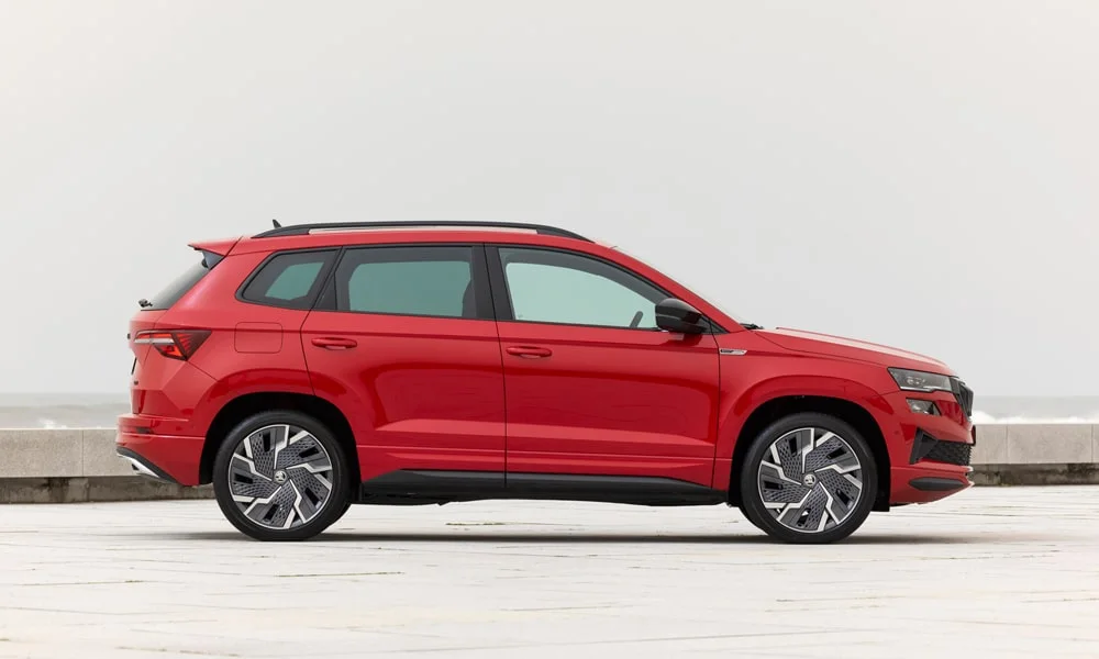 Фото Skoda Karoq (2024) — вид сбоку, фото 5. Красный кузов в профиль — пропорции, высота посадки и дизайн дисков. Хромированные или чёрные молдинги окон отличают комплектации Skoda Karoq (2024) — вид сбоку, фото 5
