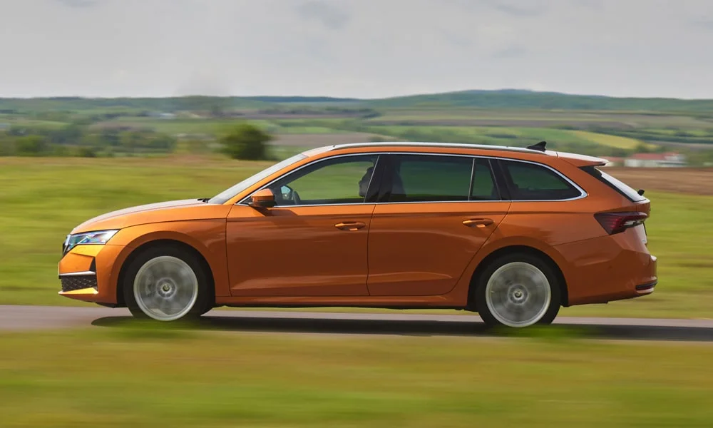 Фото Skoda Octavia Combi (2024) — вид сбоку, фото 3. Оранжевый кузов в профиль — пропорции, высота посадки и дизайн дисков. Хромированные или чёрные молдинги окон отличают комплектации Skoda Octavia Combi (2024) — вид сбоку, фото 3
