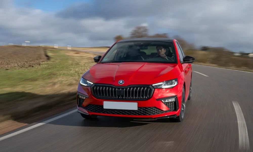 Фото Skoda Scala (2024) — вид спереди, фото 11. Кузов в красном цвете: рисунок оптики и решётки задаёт узнаваемое «лицо» модели. Рисунок ходовых огней — подпись модели, по нему её узнают в потоке Skoda Scala (2024) — вид спереди, фото 11