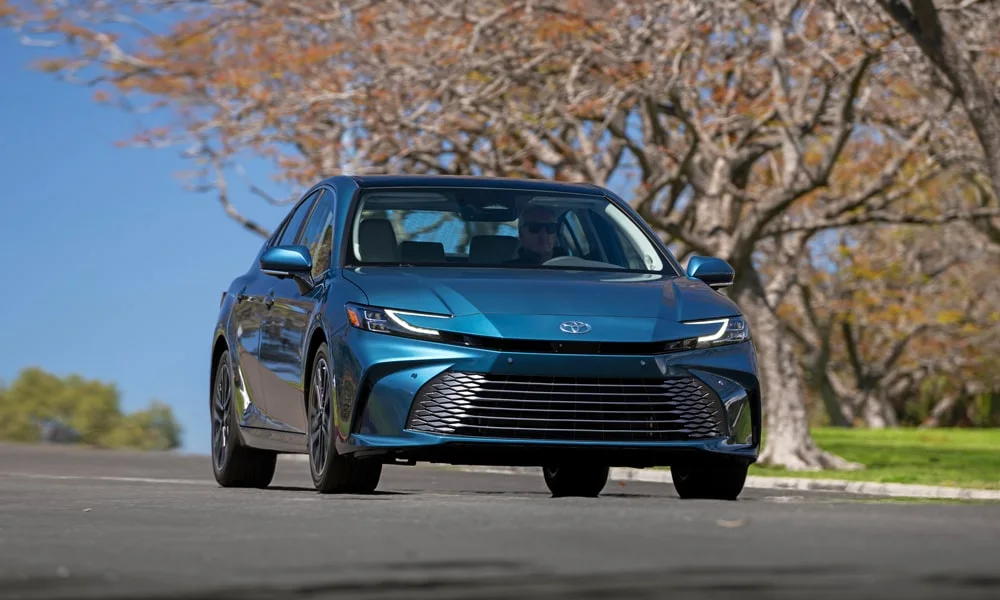Фото Toyota Camry (2024) — вид спереди, фото 8. Синий кузов, строгая симметрия оптики — базовый ракурс знакомства с дизайном. Рисунок ходовых огней — подпись модели, по нему её узнают в потоке Toyota Camry (2024) — вид спереди, фото 8